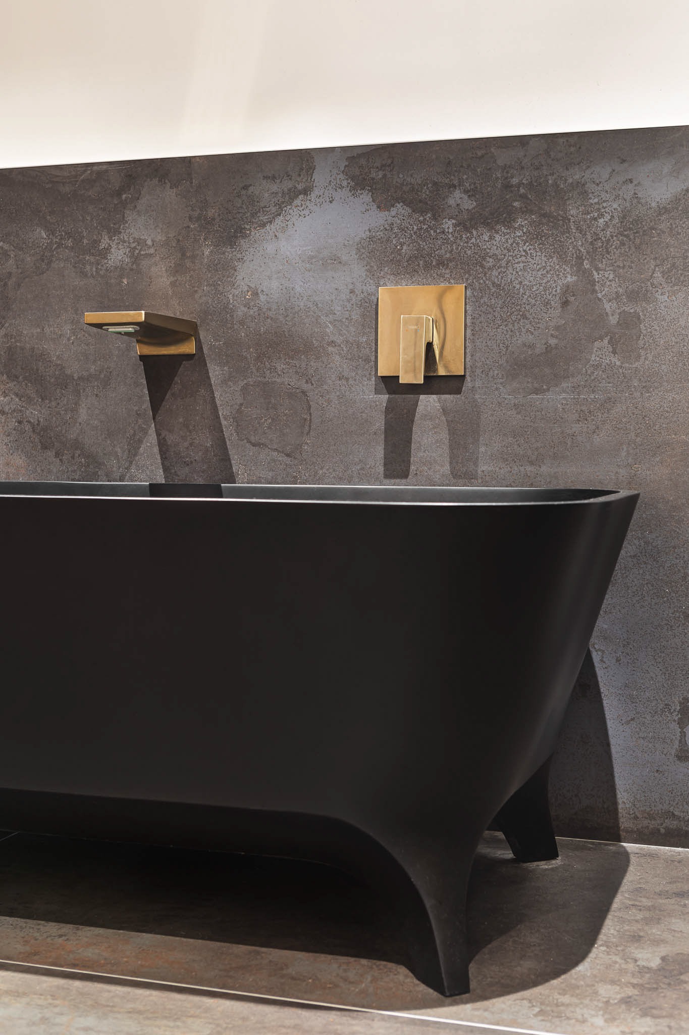 Gros plan sur une baignoire noire mate avec robinetterie dorée murale.