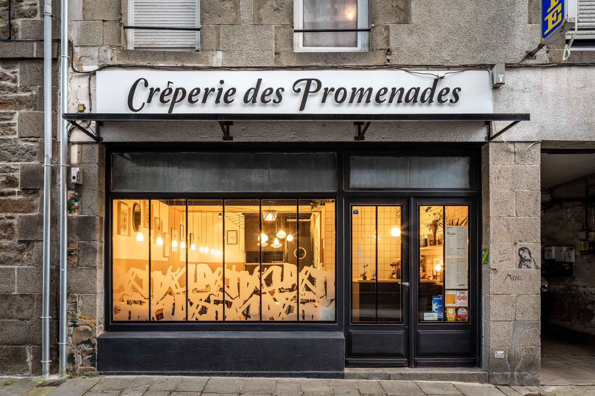 Devanture de la Crêperie des Promenades à Saint-Brieuc, avec aperçu de l’éclairage intérieur chaleureux à travers les vitres.