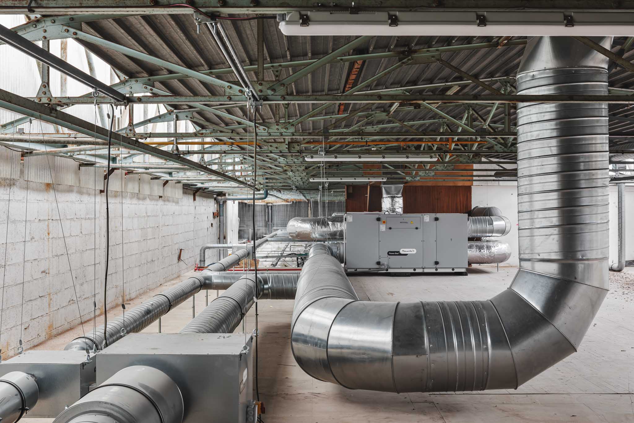 Vue des gaines de ventilation installées au plafond, illustrant le réseau de traitement d’air mis en place dans l’usine.