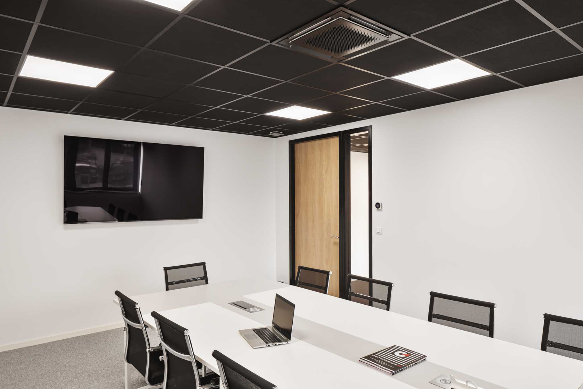Salle de réunion lumineuse avec dalles LED au plafond et chauffage par panneaux rayonnants intégrés.